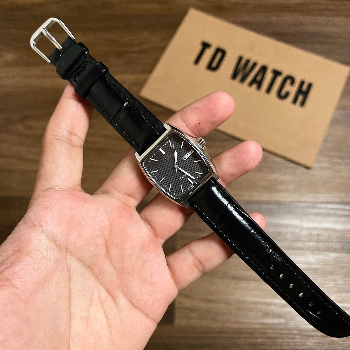 TD Watch Men's Square Black Dial Quartz Watch held in hand with TD Watch box in background